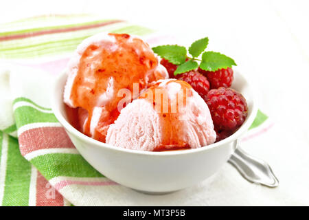 La crème glacée à la framboise rouge, les petits fruits et le sirop de menthe dans un bol blanc, une cuillère sur serviette sur planche de bois contexte Banque D'Images