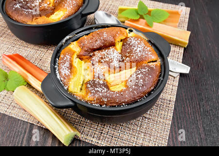 Clafouti tarte à la rhubarbe dans le brasero, menthe et tiges de rhubarbe sur une serviette sur l'arrière-plan de planche de bois Banque D'Images