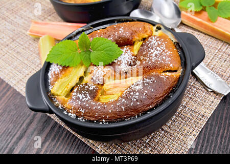 Clafouti à la rhubarbe tarte à la rhubarbe et menthe brazier, tiges sur une serviette marron sur planche en bois historique Banque D'Images