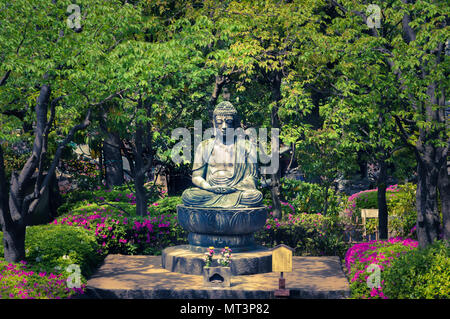 Méditante bouddhiste statue entourée d'arbres, buissons et fleurs. Banque D'Images