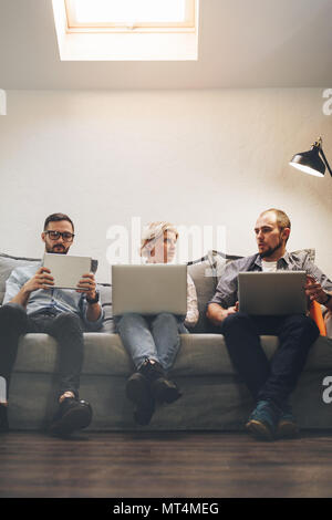 Groupe de trois collègues de travail se trouve sur la table et est titulaire d'ordinateurs portables et tablet. Les gens d'affaires travaillant dans loft Banque D'Images