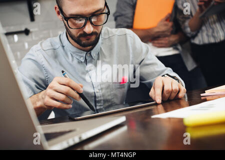 Les jeunes barbus trader analyses et études de marché de l'investissement. L'homme est sur le plan de dessin tablette avec stylet. L'utilisation de gadgets et des dispositifs électroniques dans les bu Banque D'Images