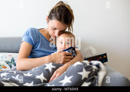 Jeune mère, tenant son bébé garçon enfant malade dans les bras, assis sur un canapé dans la salle de séjour à la maison Banque D'Images