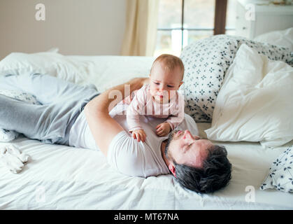 Père avec un bébé fille sur le lit chez lui à l'heure du coucher. Banque D'Images