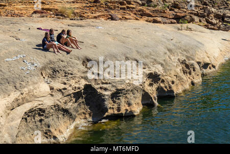 Quatre jeunes gens assis sur un rocher à côté de la rivière Lennard, Gibb River Road , Kimberley, WA, Australie. Banque D'Images