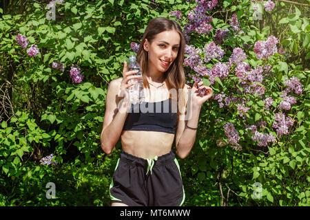 Jeune, belle femme est engagé dans le sport et des boissons de l'eau propre dans un jardin en fleurs Banque D'Images