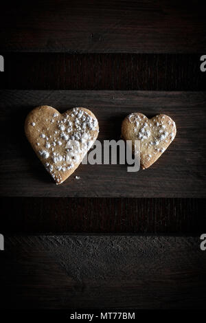 Deux délicieux cookies en forme de cœur saupoudrée de sucre glace dans une planche de bois. Vertical image vu du dessus.Concept d'amour en couple. D Banque D'Images