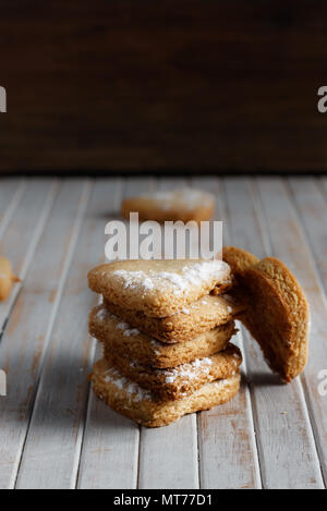 Délicieux cookies en forme de cœur saupoudrée de sucre glace dans une planche de bois. Vertical image Dark moody style. Banque D'Images