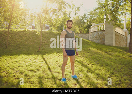 Un coureur guy se tient dans le parc au coucher du soleil. Banque D'Images