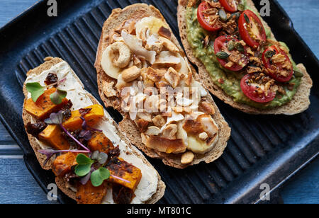 L'angle d'une grande variété de délicieux sandwichs face ouverte avec un assortiment d'ingrédients dans une poêle sur une table en bois bleu Banque D'Images