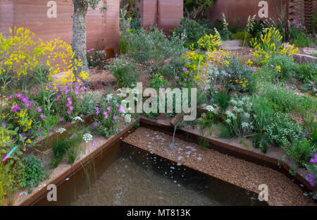 Un petit ruisseau alimentant un étang entouré de plantes y compris Isatis tinctoria (pastel), Daucus gingidium, Cistus creticus, Ridolfia segetum dans le M&G Gard Banque D'Images