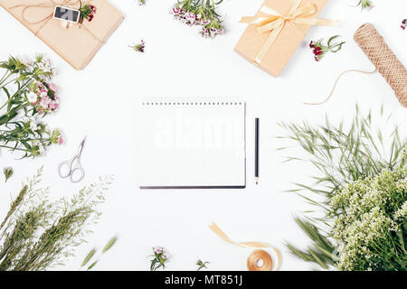 Vue de dessus du blank notepad parmi d'été à l'extérieur de fleurs et cadeaux sur fond blanc. Mise à plat maquette floral avec de l'espace pour le texte sur la feuille blanche de Banque D'Images