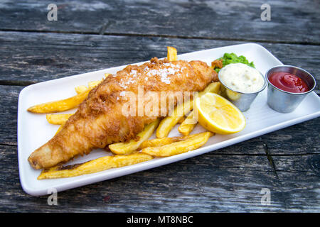 Assiette de poisson pané et frites avec petits pois et sauce tartare servi sur une table en bois Banque D'Images