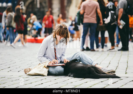 République tchèque, Prague, 25 juillet 2017 : une belle jeune femme peintre est assis sur le sol au milieu de la place et nulles, à côté d'elle se trouve un blac Banque D'Images