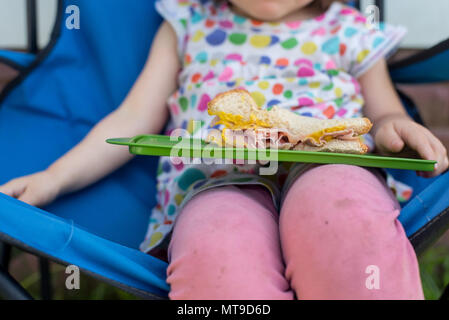 Un bébé fille tenant un sandwich au jambon à l'extérieur Banque D'Images