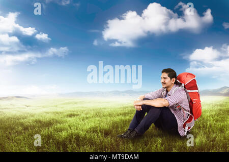 Happy traveler man with backpack assis et reposant sur le champ vert Banque D'Images