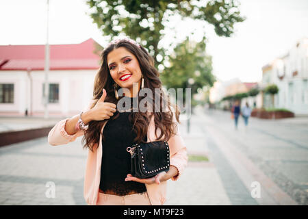 Beautiful happy girl avec sac à main noir à la mode showing thumb up. Banque D'Images