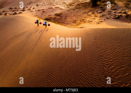 Vue aérienne de femme exerçant son panier de fleurs au coucher du soleil dans les dunes de sable de Mui Ne, Vietnam Banque D'Images