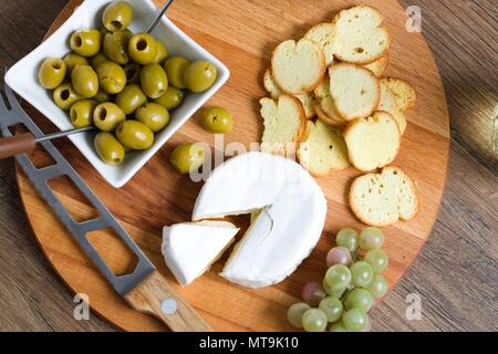 Vue du haut vers le bas sur la pâte molle à croûte blanche (camembert ou brie) sur planche de bois avec des tranches de pain grillées, les olives et les raisins. Pièce en forme de triangle o Banque D'Images