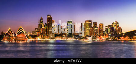 De soleil colorés sur la ville de Sydney CBD waterfront comme vu à travers les eaux troubles du port de Sydney reflétant les lumières vives des bâtiments illuminés. Banque D'Images