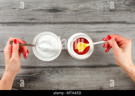 Vue supérieure de la jeune femme sur les mains avec des clous rouges, holding spoon plein de sucre et de miel dans un autre côté. Vs Sucre Miel concept. Banque D'Images