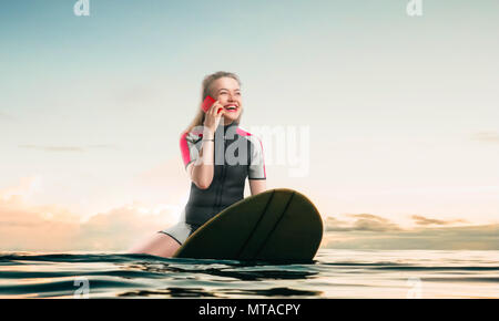 Velo femme windsurfer en wetsuit siégeant au conseil et des entretiens par téléphone Banque D'Images