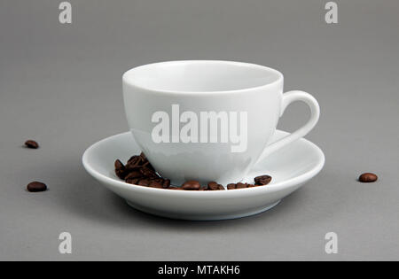 Café en grains s'échappant d'une tasse de café sur fond gris Banque D'Images