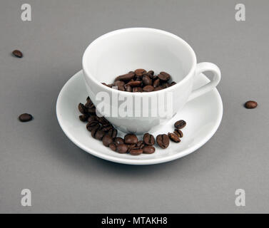 Café en grains s'échappant d'une tasse de café sur fond gris Banque D'Images