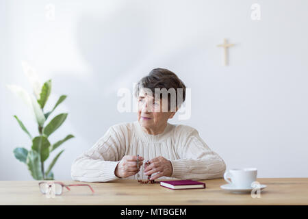 Femme âgée religieux plein de foi prier avec un chapelet à une table avec bible Banque D'Images