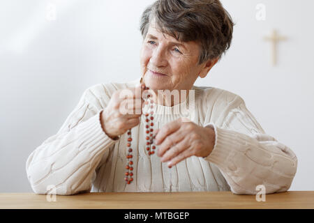 Portrait of smiling grandmother with red rosaire prier dans l'église Banque D'Images