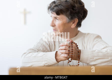 Hauts femme en prière avec un chapelet dans une église catholique lumineux Banque D'Images