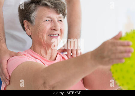 Femme âgée en compagnie de ses exercices isométriques avec une balle de massage dopés, jaune Banque D'Images