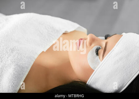 Portrait of Girl salon au cours de procédure d'extension des cils. Jeune femme avec jolie visage allongé sur une headbandage lashmaking pour porter l'entraîneur. Aimer beaty procédures. Banque D'Images