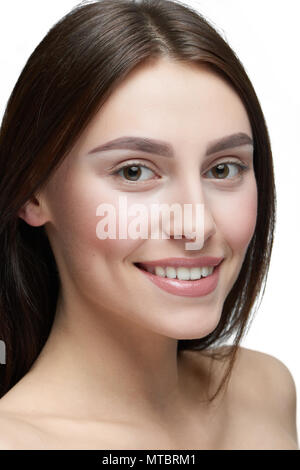 Close up of a Girl avec lumière jour composent looking at camera. modèle avoir beau visage avec beau sourire, lèvres charnues, de grands yeux, des dents blanches. Des cheveux bruns foncés, a ouvert les épaules. Studio blanc arrière-plan. Banque D'Images