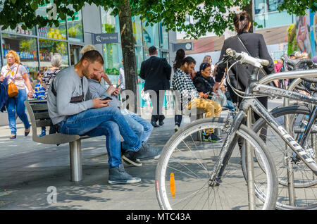 Les vélos garés dans un support à bicyclettes à côté de bancs avec les gens se préoccupe de leur téléphone mobile, Banque D'Images