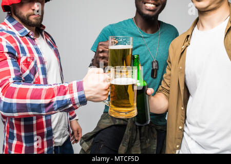 Près de trois jeunes hommes heureux de trinquer avec des verres de bière isolé sur gray Banque D'Images