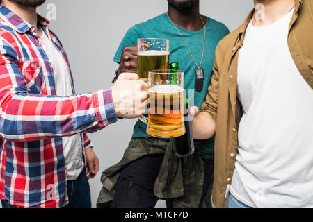 Près de trois jeunes hommes heureux de trinquer avec des verres de bière isolé sur gray Banque D'Images