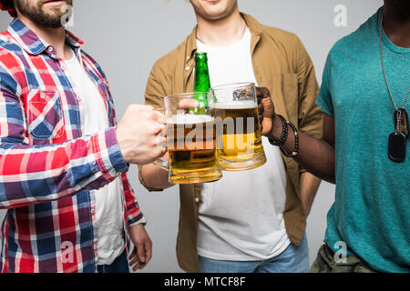 Près de trois jeunes hommes heureux de trinquer avec des verres de bière isolé sur gray Banque D'Images