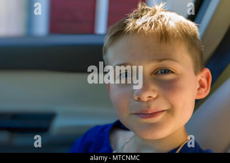 Voir portrait de jeune garçon de 10 ans dans le siège passager de voiture à and smiling at camera Banque D'Images