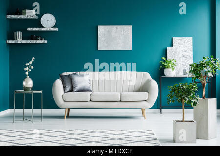 Canapé blanc entre une table en métal et un bureau noir avec des peintures et des plantes dans un salon intérieur turquoise Banque D'Images