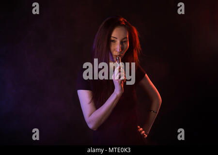 Jeune femme fumant cigarette électronique sur fond sombre Banque D'Images