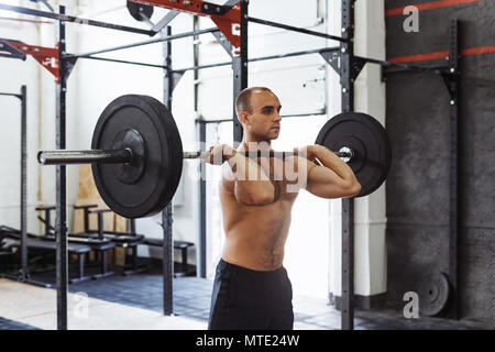 Coup de jeune homme musclé faisant squats avec barbell in a gym Banque D'Images