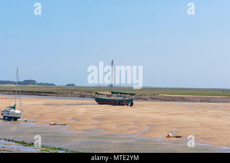 Un vieux yacht est assis sur un banc de sable à marée basse dans un estuaire. Dans les marais salants de la distance Banque D'Images