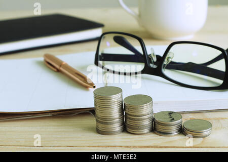 Pile d'argent et un stylo et verres jeter sur carnet de notes sur la table de travail. Banque D'Images