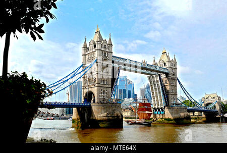 Voir à partir de la rive sud de la Tamise avec le Tower Bridge soulevées et voilier 'Eye of the wind' passant en dessous. Ville de London bâtiments en arrière-plan Banque D'Images