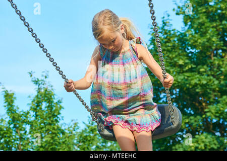 Petit enfant fille blonde s'amusant sur une balançoire à l'extérieur. Jeux d'été. Fille se balançant de haut. Jeune enfant sur la balançoire en plein air. Banque D'Images