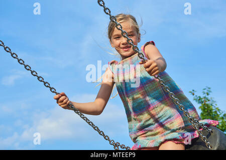 Petit enfant fille blonde s'amusant sur une balançoire à l'extérieur. Jeux d'été. Fille se balançant de haut. Jeune enfant sur la balançoire en plein air. Banque D'Images