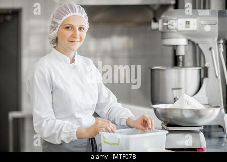 Portrait d'une femme en uniforme confiseur pesant ingrédients pour la fabrication à la boulangerie pâtisserie Banque D'Images