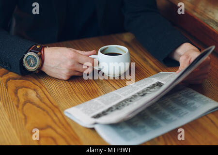 Man's hands close-up holding tasse de café et un journal sur une table en bois. Businessman en costume et vintage watch la lecture des nouvelles tout en tenant une whit Banque D'Images