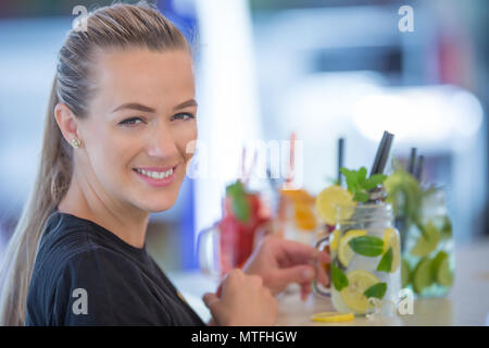 Jolie jeune femme avec un beau sourire tout en travaillant dans un bar la préparation de limonades. Banque D'Images